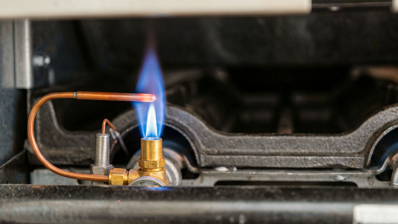 Close-up view of a lit furnace pilot light with a steady blue flame near the igniter assembly.