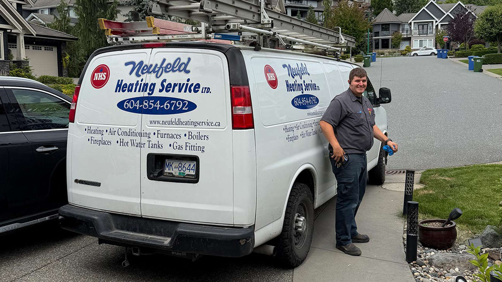 Friendly Neufeld Heating technician standing next to a company service van parked outside a residential home in Abbotsford.