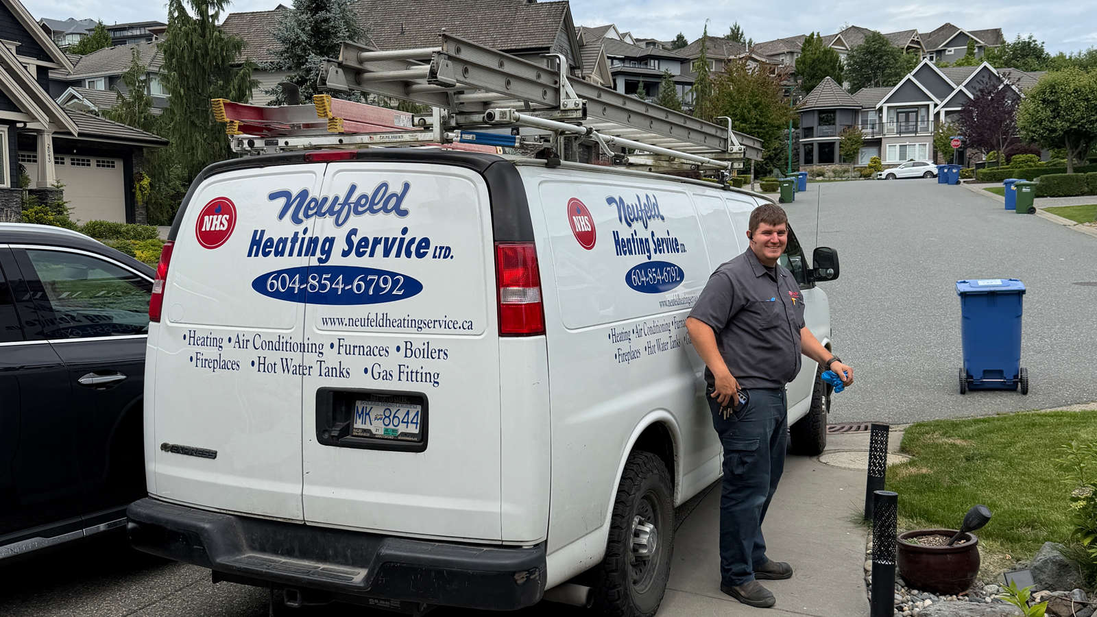 Neufeld Heating technician standing outside near a company service van parked in an Abbotsford neighborhood.