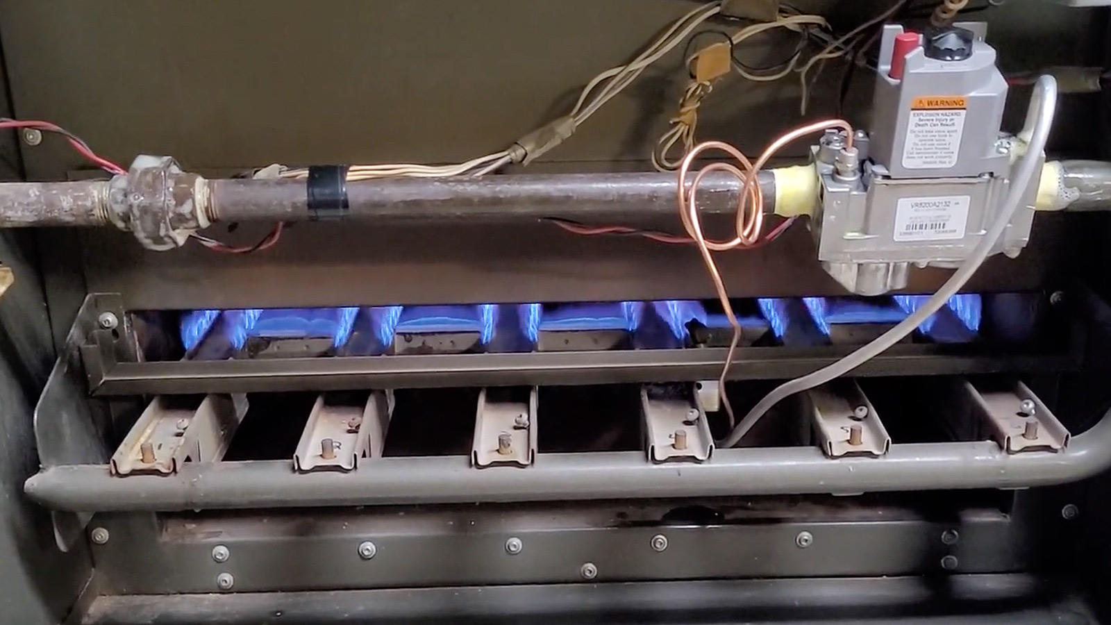 Close-up of internal gas fireplace maintenance components showing active blue burner flames and control valve assembly.